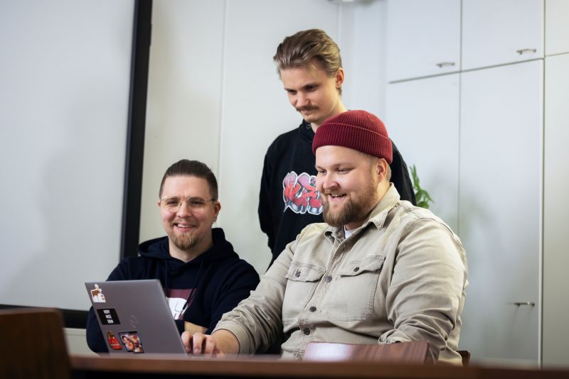 Three Hurja employees are looking at a laptop in the meeting room.