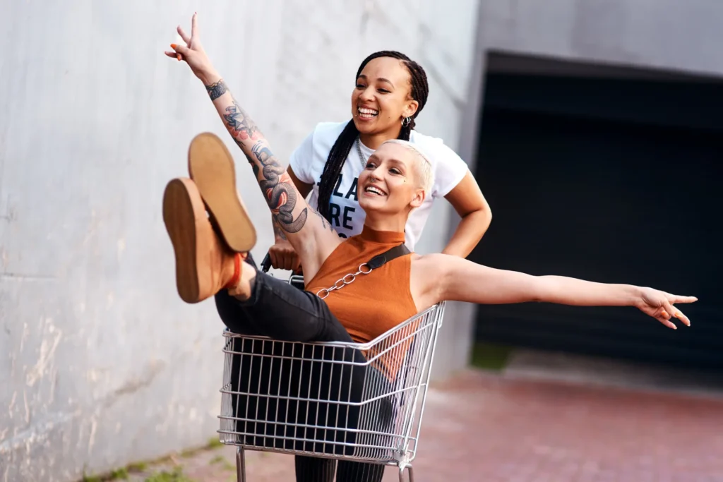 Kaksi nuorta naista ajaa iloisina ostoskärryllä, symboloiden verkkokauppoja ja digipalvelulain tuomia saavutettavuusvaatimuksia, jotka koskevat kaikkia käyttäjiä.