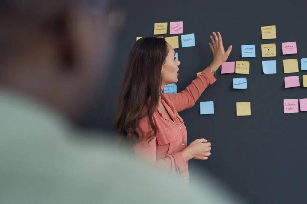 Käyttäjätarinat artikkelin kansikuva, jossa nainen esittelee suunnitelmaa postitlapuilla.