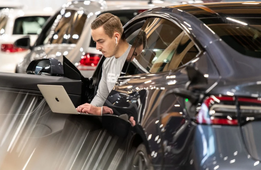 Mies työskentelee kannettavalla tietokoneella autossa Sakan autoliikkeessä.